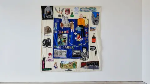 Joseph Horton A colourful tapestry hanging on a white wall with a blue centre and images of the 1980s and Sheffield