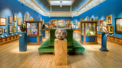 The new Upper Gallery space with artworks and sculptures and a green sofa in the middle. The walls have been painted a bright royal blue.