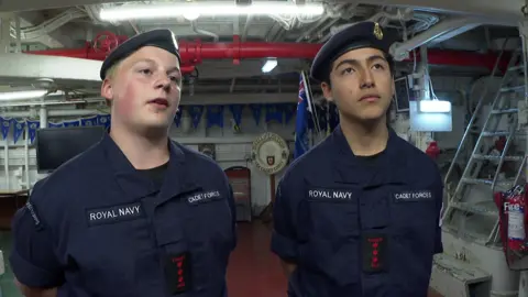 Two teen boys wearing cadet uniforms on board a warship