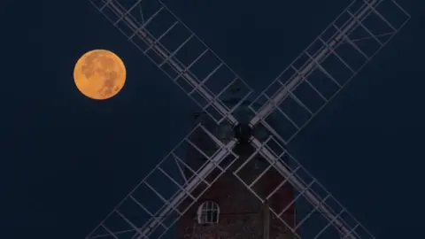 BBC Weather Watchers/Coastal JJ Ang supermoon makita sa luyo sa mga blades sa usa ka karaang windmill sa Selsey, West Sussex.