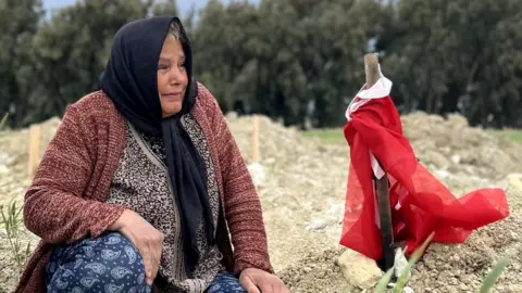 Wietske Burema/BBC Fethiye Keklik mourns her son next to a Turkish flag