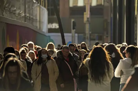 PA Media Dozens of shoppers walk along a street in Belfast