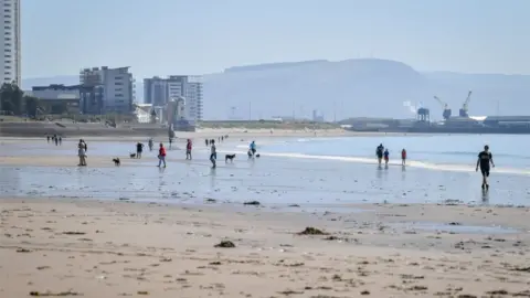 PA Media People walk along the beach in hot weather in Swansea, Wales