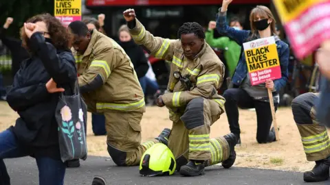 Getty Images A firefighter in uniform kneels during the protest