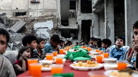 European Photopress Agency Children sit at a table as they wait for Iftar, evening meal at the end of daily Ramadan fast at sunset, next to rubble and destroyed houses, which were damaged after air strikes, in Douma, Syria, 17 June 2017.