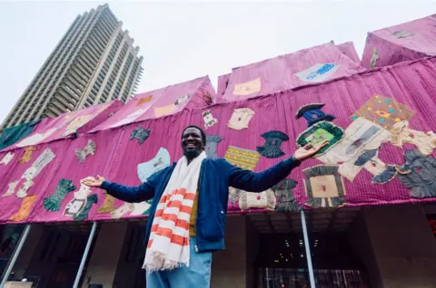 BENJAMIN CREMEL/AFP Ghanaian artist Ibrahim Mahama poses for a photograph in front of his installation entitled 'Purple Hibiscus' at the Barbican centre in central London on April 9, 2024.