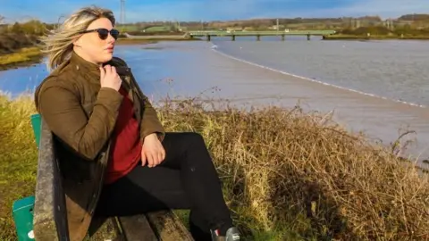 Debbie Burrows Laura Mathias in a wig on a bench in manningtree