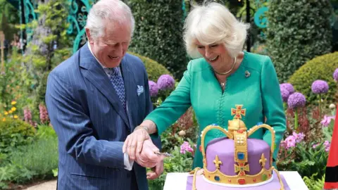 Reuters King Charles and Queen Camilla cut cake at visit to a newly-created Coronation Garden in Newtownabbey,