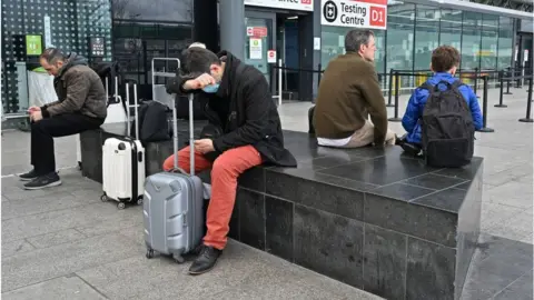 Getty Images Holidaymakers and travellers sit outside the Covid-19 Test centre at Terminal 3 of London Heathrow Airport in west London