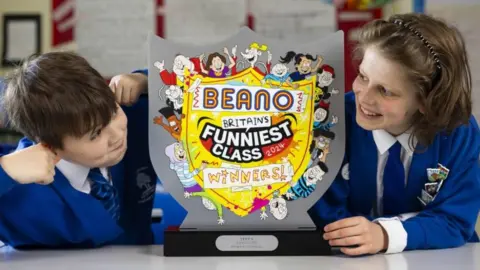 PA Media Students Anthony Floarea (left) and Gavriil Stovl from Northside Primary School pull faces as they hold the Beano trophy