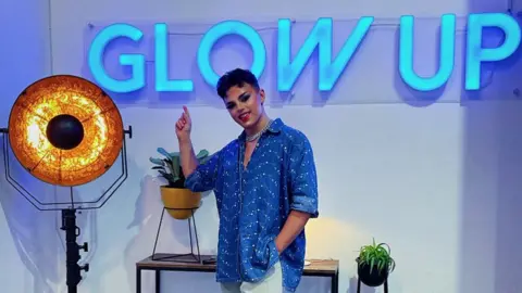 Wezley Webber Wezley Webber pointing at a neon Glow Up sign