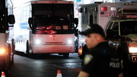 Getty Images A police man stands in front of a bus carrying migrants that is arriving in New York City from Texas.