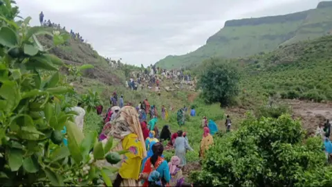 AFP A view of lots of people in a lush valley. They all have their backs to the camera and looking at the aftermath of the landlside.