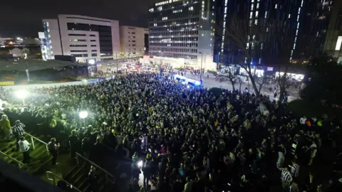 Fans afuera de St James Park por la noche. Muchas camisas blancas.