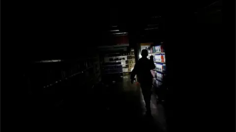 Reuters A worker inspects damage in a supermarket after it was looted during an ongoing blackout in Caracas, Venezuela March 10, 2019.