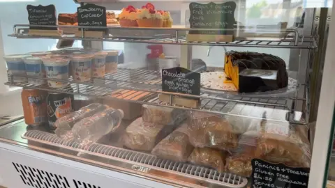 Ollie Conopo/BBC A food counter with sandwiches, cakes, yogurt and soft drinks.