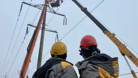 Daria Sipigina Two men in hard hats looking at a pylon