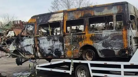 Burnt out school minibus being lifted onto a trailer