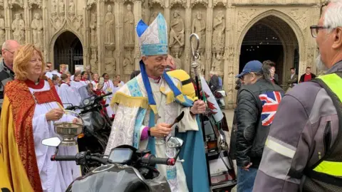 The bishop in his traditional clothing outside the building blessing bikers. 