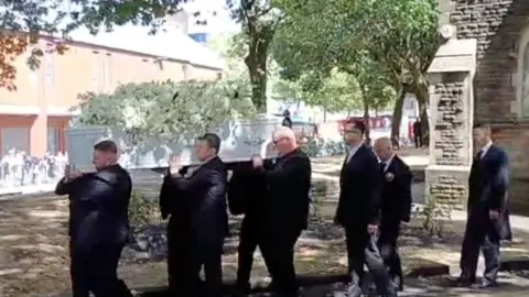 Pallbearears carrying a white coffin carrying white flowers out of a church