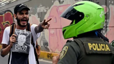 AFP A demonstrator holding a poster of the late Dilan Cruz shouts at riot police during a march against the government of Colombian President Ivan Duque during a national strike in Cali on November 27, 2019