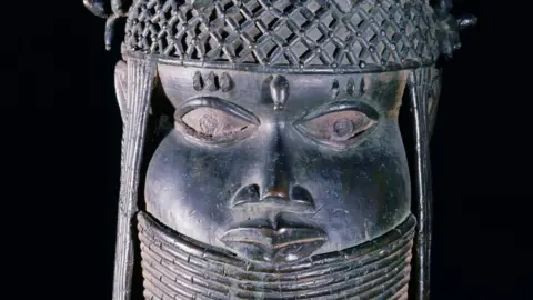 Getty Images A head of an oba from an ancestral shrine. The head has a high coral collar and a beaded cap with coral clusters in British Museum collection