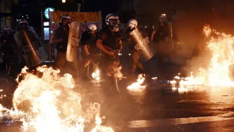 Getty Images Riot police stand amid petrol bombs threw by protesters during an anti-austerity protest on July 15, 2015.