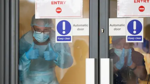 Reuters Medical staff in PPE clap through a glass door