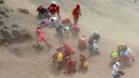 EPA 0 A handout photo made available by Agencia Andina shows a group of emergency personnel covering themselves from dust generated by a helicopter during rescue operatons after a passenger bus plunged off the Pan-American Highway North, about 45 kilometers from Lima, Peru, 02 January 2018