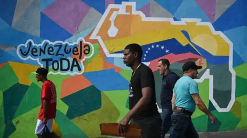 Getty Images People walk by a mural campaigning for a referendum to ask Venezuelans to consider annexing the Guyana-administered region of Essequibo, in 23 de Enero neighbourhood in Caracas on November 28, 2023.