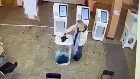 Reuters A woman pours a liquid into a ballot box, during the Russian presidential election in Moscow, Russia, in this screen grab taken from a video recording of a screen showing CCTV footage, March 15, 2024