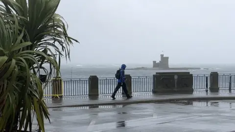 BBC Man walking by Bottle Neck car park in stormy weather