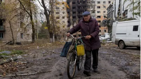 Reuters A man walks with bicycle in front of damaged residential buildings in Avdiivka, eastern Ukraine. File photo