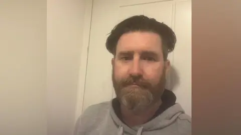 Supplied A selfie of a man wearing a grey hooded top. He is standing in front of a white door.