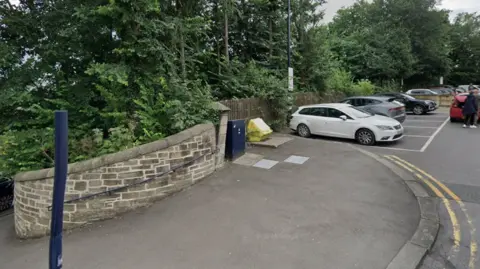Pavement outside Durham train station in Station Approach. There is a large stretch of pavement which is next to a row of car parking places which are filled. 
