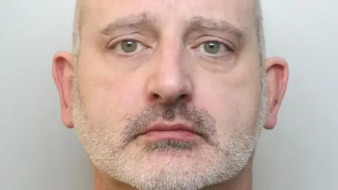 Police mugshot of Lee Smith, who has shaved grey hair and grey stubble.