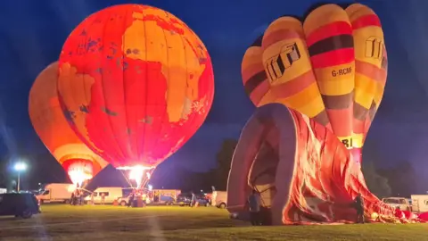 Dan Whitelock/Bristol Balloon Collectors Three hot air balloons in the night in a park