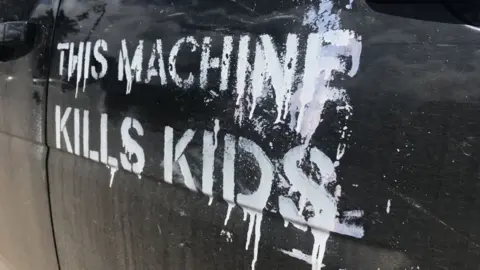 A car spray painted with the slogan 'This machine kills kids' in white paint