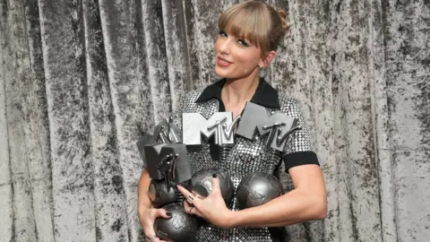 Getty Images Taylor Swift in a sparkly dress, holding three MTV EMA awards