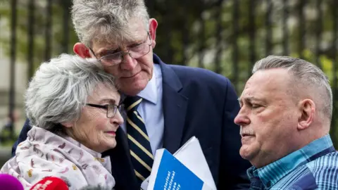 PA Kate McCausland is embraced by Jon McCourt and accompanied by John Heaney