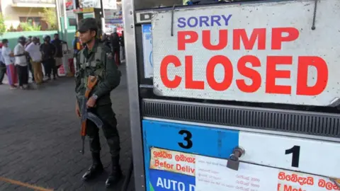 Getty Images A Sri Lankan security personnel stands guard outside a fuel station in Colombo.