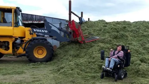 Glenda Turtle Jonathan Turtle in his wheelchair beside a silage pit