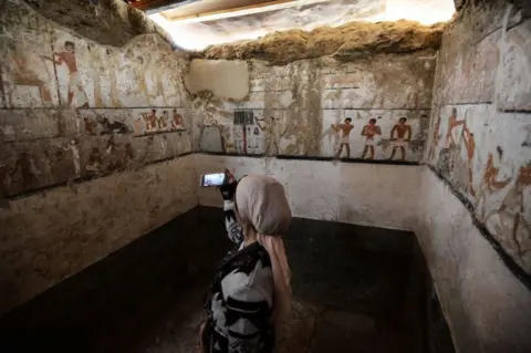 AFP A woman takes a photo inside the tomb of an Old Kingdom priestess adorned with well-preserved and rare wall paintings on the Giza plateau in Cairo that was unveiled on February 3, 2018 after being discovered during excavation work in Giza's western cemetery by a team of Egyptian archaeologists. Antiquities Minister Khaled al-Enany told reporters the tomb belong to Hatpet, a priestess to Hathor, the goddess of fertility who assisted women in childbirth.