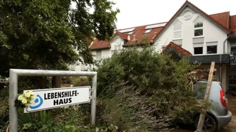 Getty Images A large building with white walls and a red roof. A large amount of wood, mud and debris can be seen outside it