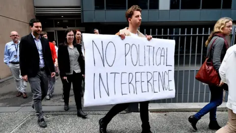 EPA Journalists walk of the ABC in Sydney, with one carrying a 'No political interference' sign
