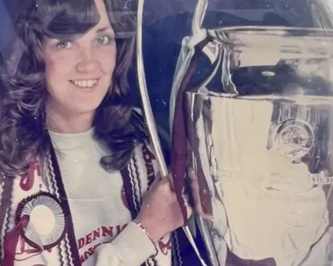 A young woman with an early-1980s hairstyle and draped in a Villa scarf poses with the European Cup 44 years ago