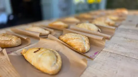 Pasties laid out on brown grease-proof paper on a wooden table.