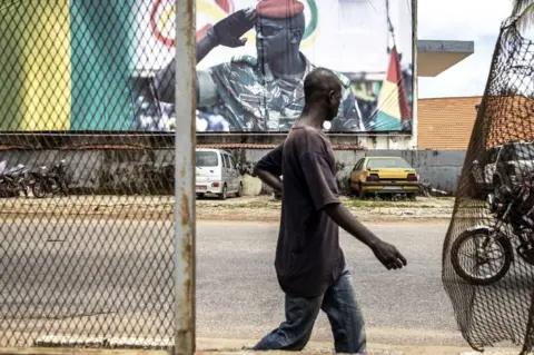AFP A man walks past a billboard showing junta leader Col Mamady Doumbouya on 11 September.