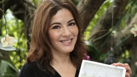 Getty Images Nigella Lawson smiling as she holds her cookbook.
