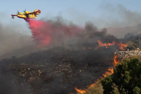 Antonio Cascio / Reuters An aircraft drops flame retardant on burning vegetation in Sicily